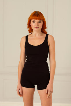 Woman stood faced forwards wearing thine organics black cotton cami vest and boxer shorts